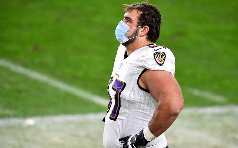 Raven player on sidelines with COVID mask on